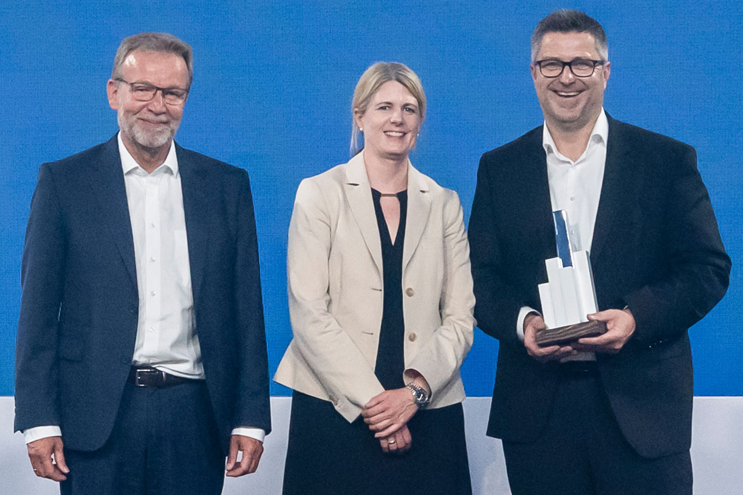 Ein fröhlicher Andreas Gründemann mit seinem Award neben den beiden Gratulanten, Axel Wilhelm in Vertretung der Jury und Christina Volkmann vom Sponsor Nuveen.
