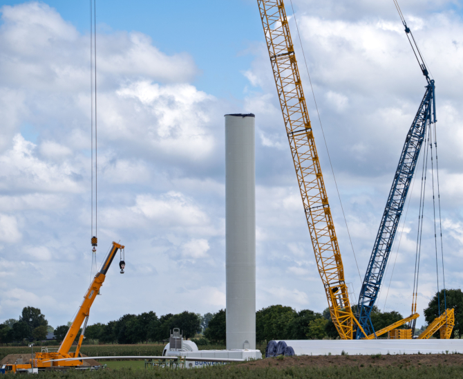 Kräne montieren einen Windkraftturm in einem offenen Feld unter einem bewölkten Himmel.